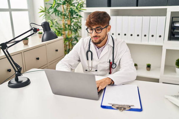 Young arab man wearing doctor uniform using laptop working at clinic - Foto, immagini