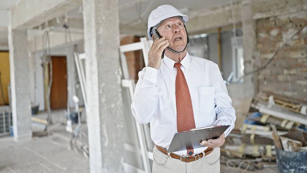 Älterer grauhaariger Mann telefoniert mit Smartphone und schaut sich auf Baustelle um - Foto, Bild