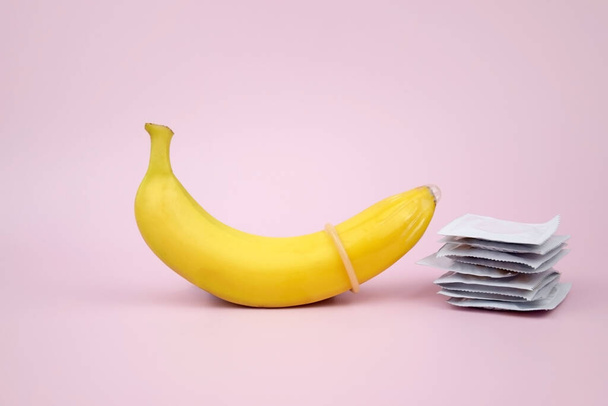 Condoom en banaan op een roze achtergrond close-up. Het begrip seksuele gezondheid. - Foto, afbeelding