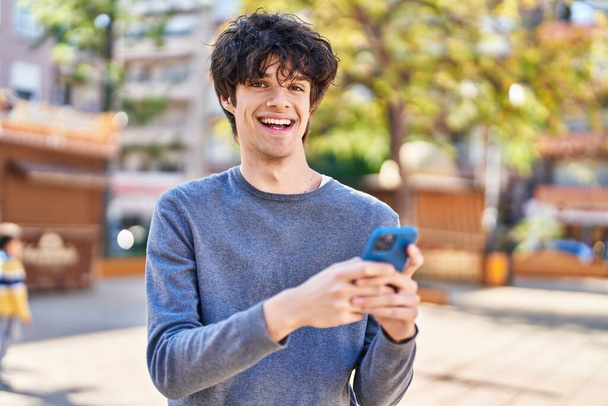 Parkta akıllı telefon kullanarak gülümseyen İspanyol genç adam. - Fotoğraf, Görsel