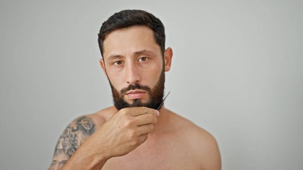 jonge latino man kammen baard staan shirtless over geïsoleerde witte achtergrond - Foto, afbeelding