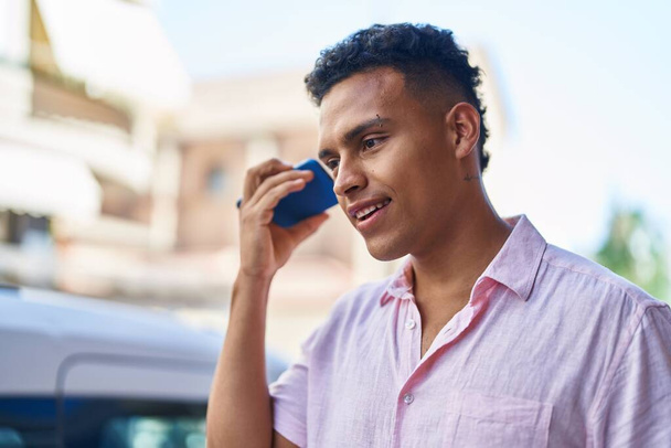 Νεαρός Λατίνος άνθρωπος χαμογελά αυτοπεποίθηση ακούγοντας ηχητικό μήνυμα από το smartphone στο δρόμο - Φωτογραφία, εικόνα