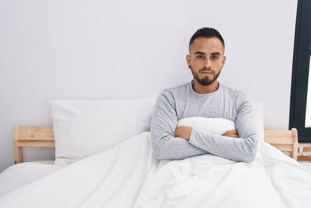 Jeune homme hispanique couché sur le lit avec une expression sérieuse dans la chambre - Photo, image