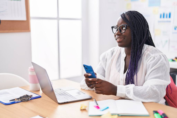 オフィスでノートパソコンやスマートフォンを使っているアフリカ系アメリカ人女性ビジネスワーカー - 写真・画像
