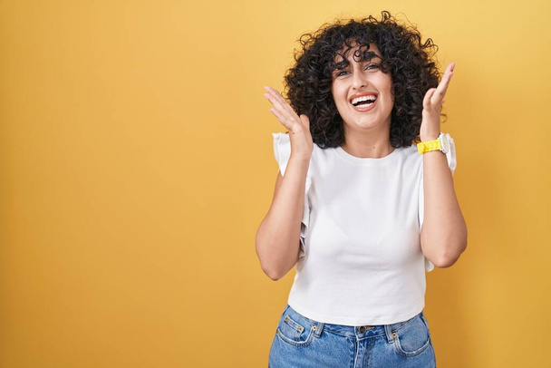Νεαρή γυναίκα της Μέσης Ανατολής στέκεται πάνω από κίτρινο φόντο γιορτάζει τρελό και κατάπληκτος για την επιτυχία με τα χέρια υψωμένα και ανοιχτά μάτια ουρλιάζοντας ενθουσιασμένος. έννοια νικητή  - Φωτογραφία, εικόνα