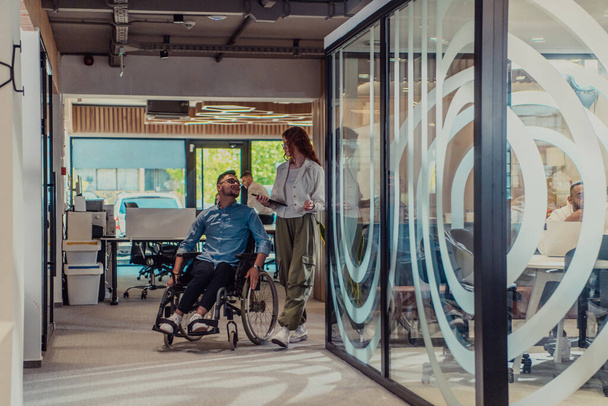 Young business colleagues, collaborative business colleagues, including a person in a wheelchair, walk past a modern glass office corridor, illustrating diversity, teamwork and empowerment in the - Foto, imagen