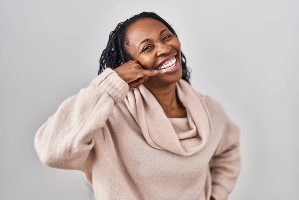Африканская женщина, стоящая на белом фоне, улыбаясь, делает телефонный жест рукой и пальцами, как будто разговаривает по телефону. коммуникационные концепции.  - Фото, изображение
