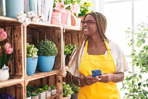 Африканська американська жінка флористка посміхається впевнено, використовуючи смартфон для флориста. - Фото, зображення
