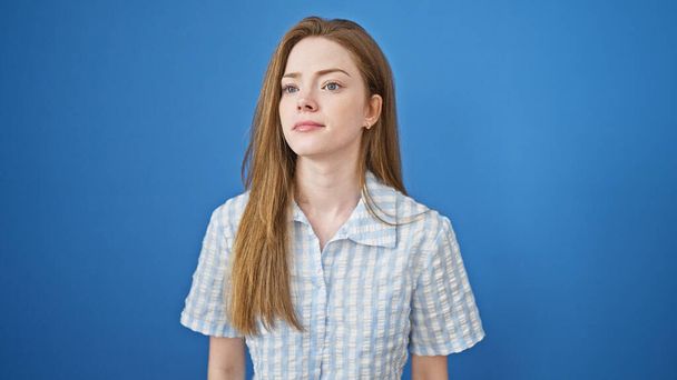 Jeune femme blonde debout avec une expression sérieuse sur fond bleu isolé - Photo, image