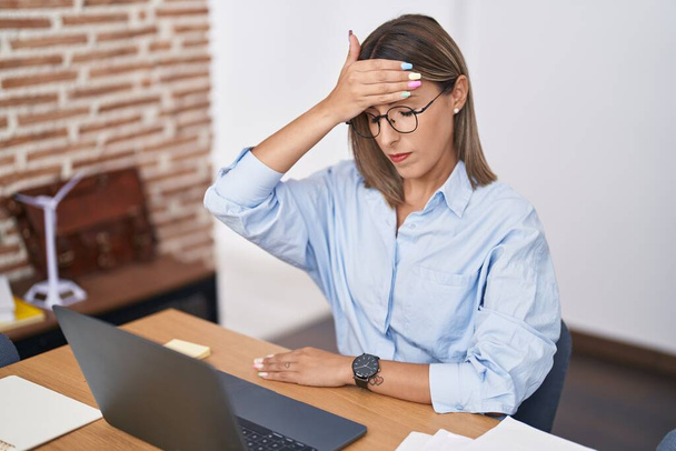 Νεαρή όμορφη ισπανόφωνη επιχειρηματίας χρησιμοποιώντας φορητό υπολογιστή που υποφέρει για πονοκέφαλο στο γραφείο - Φωτογραφία, εικόνα