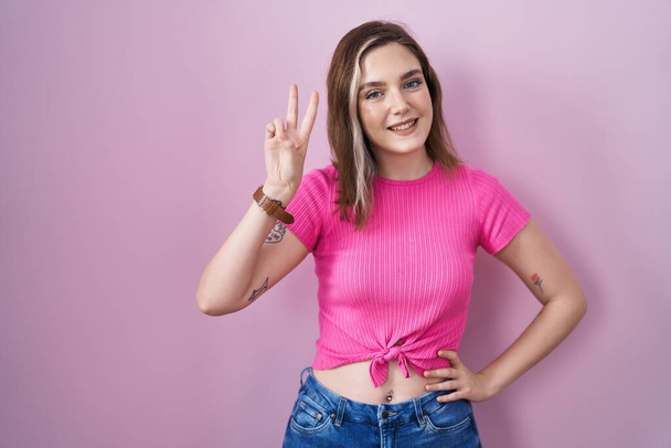 Blonde caucasian woman standing over pink background smiling looking to the camera showing fingers doing victory sign. number two.  - Photo, Image