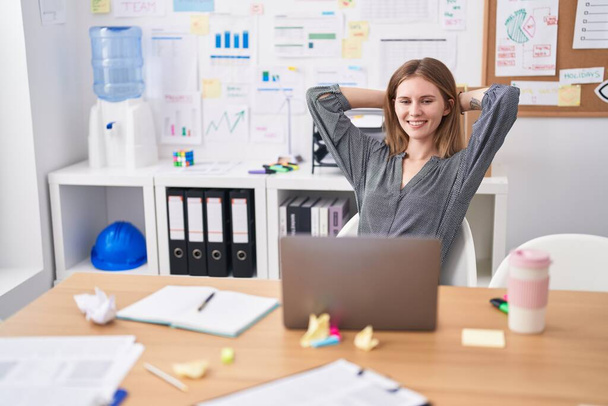 Fiatal szőke nő üzleti dolgozó laptopot használ lazán, kezekkel a fején az irodában - Fotó, kép