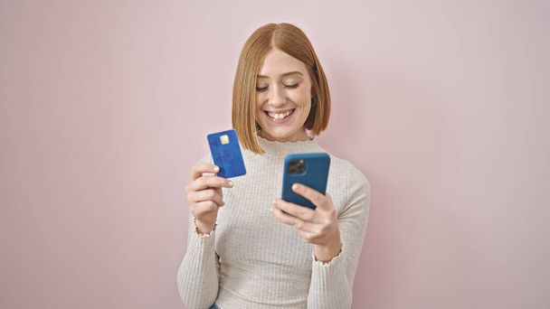 Giovane donna bionda shopping con smartphone e carta di credito su sfondo rosa isolato - Foto, immagini