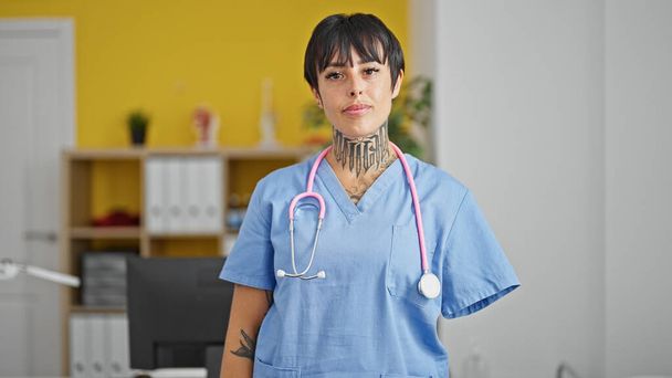 Mulher hispânica com médico braço amputado de pé com expressão séria na clínica - Foto, Imagem