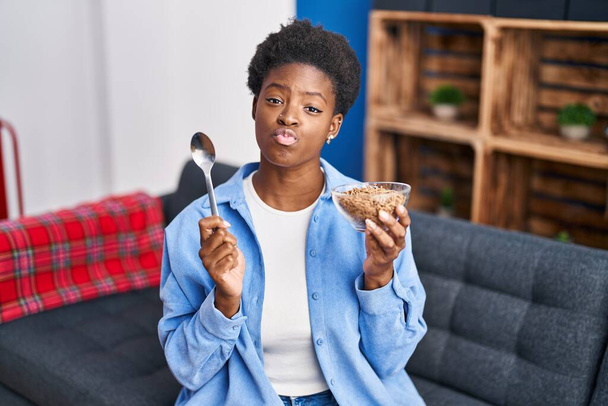 Mulher afro-americana comendo cereais integrais saudáveis olhando para a câmera soprando um beijo sendo adorável e sexy. expressão do amor.  - Foto, Imagem