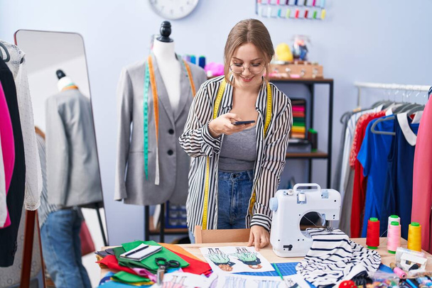 Jonge blonde vrouw kleermaker maken foto naar kleding ontwerp bij kleermaker winkel - Foto, afbeelding