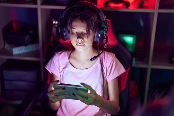 Αξιολάτρευτο ισπανόφωνο κορίτσι streamer παίζει video game χρησιμοποιώντας smartphone στο gaming room - Φωτογραφία, εικόνα