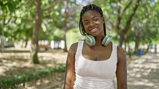 Afričanky americká žena nosí sluchátka s úsměvem v parku - Fotografie, Obrázek