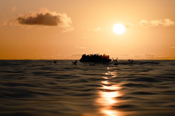 Беженцы на большой резиновой лодке посреди моря, которым нужна помощь. Море, когда люди в воде просят о помощи. Мигранты, пересекающие море
 - Фото, изображение