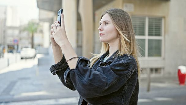 Молода блондинка робить фотографію на смартфоні на вулиці - Фото, зображення