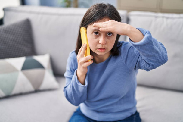 Junge Frau mit Down-Syndrom macht sich Sorgen, wenn sie zu Hause mit dem Smartphone spricht - Foto, Bild