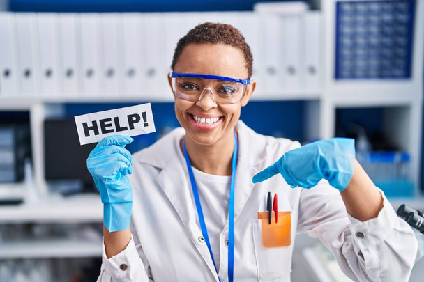 Mulher americana africana bonita trabalhando no laboratório cientista pedindo ajuda apontando dedo para um auto sorrindo feliz e orgulhoso  - Foto, Imagem