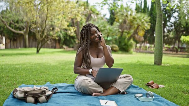 Afrikkalainen amerikkalainen nainen opiskelija käyttää laptop puhuu älypuhelimella kampuksella yliopistossa - Valokuva, kuva