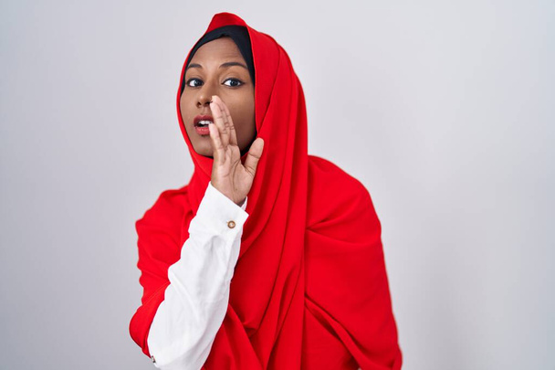 Young arab woman wearing traditional islamic hijab scarf hand on mouth telling secret rumor, whispering malicious talk conversation  - Photo, Image