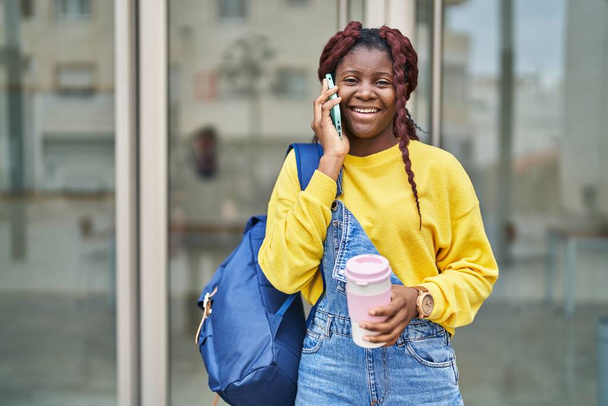 African american woman student talking on smartphone drinking coffee at university - Foto, Bild