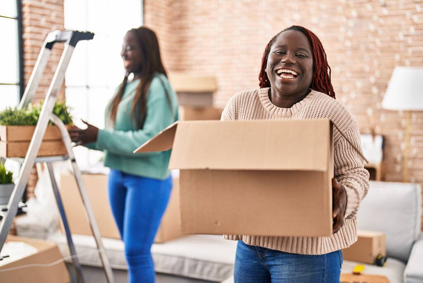 Dvě africké ženy se stěhují do nového domova s úsměvem a hlasitě se smějí, protože vtipný bláznivý vtip.  - Fotografie, Obrázek