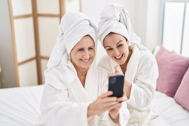 Mother and daughter wearing bathrobe having video call at bedroom - Fotó, kép