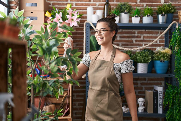 Młoda piękna latynoska kobieta kwiaciarnia za pomocą dyfuzora pracy w kwiaciarnia - Zdjęcie, obraz
