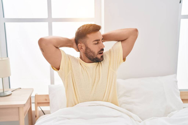 Молодий іспаномовний чоловік сидить на ліжку позіхання в спальні
 - Фото, зображення