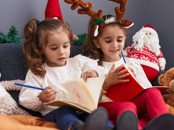 Due bambini che scrivono sul taccuino seduti sul divano per la decorazione natalizia a casa - Foto, immagini