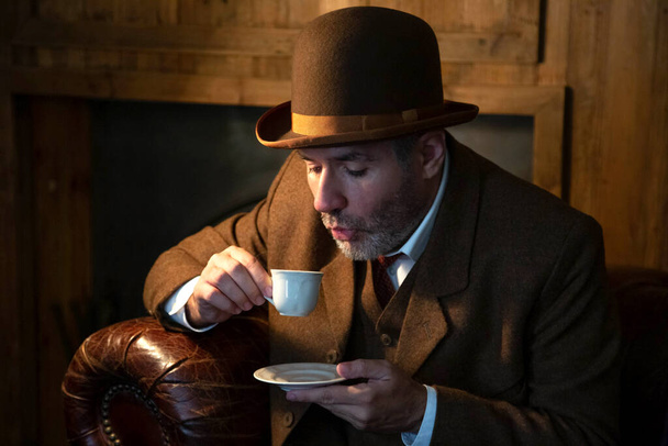 Un hombre con sombrero victoriano y traje bebe café de una taza de porcelana blanca en un salón de estilo retro. - Foto, Imagen