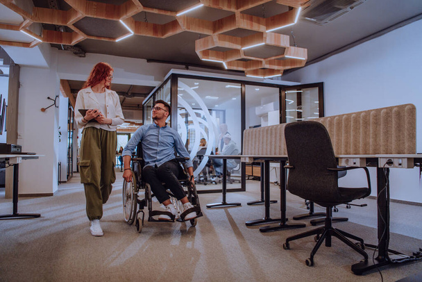 Young business colleagues, collaborative business colleagues, including a person in a wheelchair, walk past a modern glass office corridor, illustrating diversity, teamwork and empowerment in the - Фото, зображення