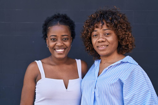 Afrikaans amerikaanse vrouwen moeder en dochter staan samen over geïsoleerde zwarte achtergrond - Foto, afbeelding