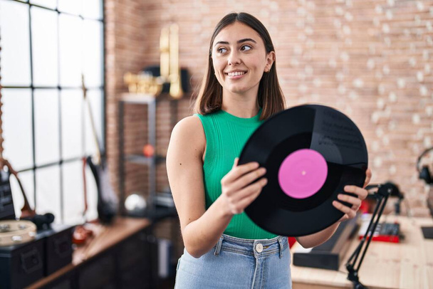 Joven mujer hispana músico sosteniendo disco de vinilo en el estudio de música - Foto, imagen