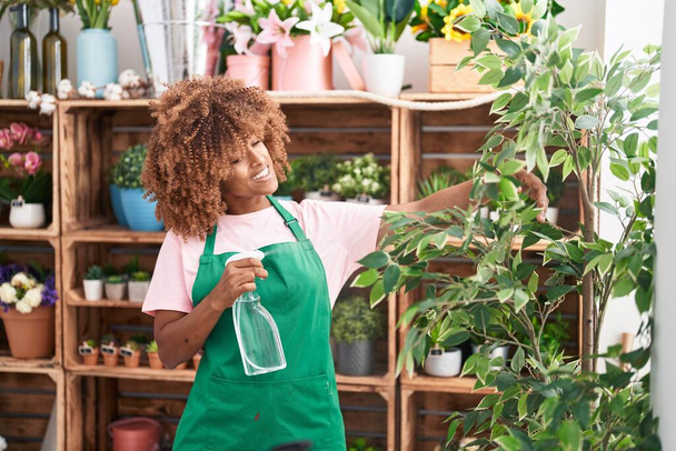 Fiorista donna afroamericana utilizzando diffusore irrigazione pianta al negozio di fiori - Foto, immagini