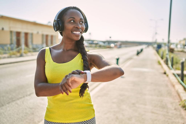 African american woman listening to music looking stopwatch at street - Photo, Image