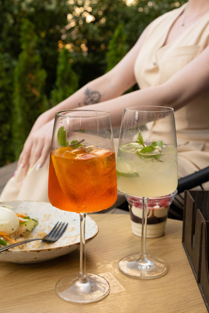 Due bicchieri di cocktail estivo con ghiaccio su un tavolo in un caffè con una donna sullo sfondo. - Foto, immagini