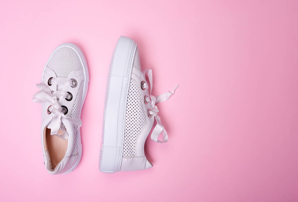 Modern white casual sneakers from perforated leather isolated on a soft pink background with copy space. Fashion blog or magazine concept. Top view - Photo, Image
