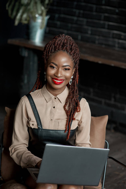 Uśmiechnięta czarna kobieta pracująca przy laptopie. Freelancer pracuje nad swoim projektem w domu. Praca online zdalnego pracownika, kobieta sukcesu konsultant, analityk, badacz lub doradca - Zdjęcie, obraz