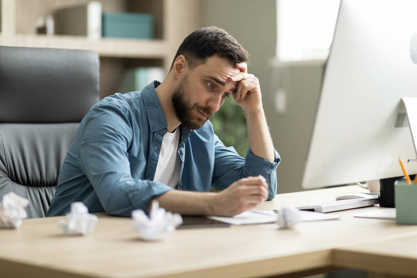 Creativity Crisis. Stressed young businessman sitting at desk in office and crumpling paper in despair, millennial male entrepreneur suffering lack of inspiration, having problems with project - Photo, Image