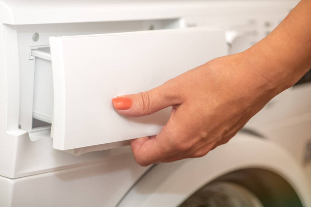 Жінка відкриває лоток для вливання прального порошку в пральну машину. Концепція прання брудного одягу в пральній машині. Використання різних миючих засобів для одягу - Фото, зображення