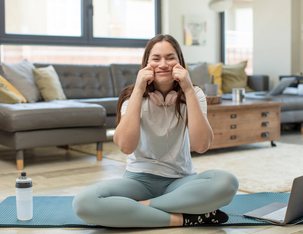young adult woman practicing yoga smiling and pointing to own fake smile - Фото, зображення
