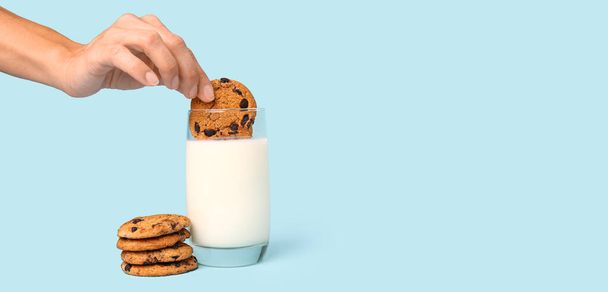 Жінка занурює смачне печиво в склянку молока на світло-блакитному фоні з місцем для тексту - Фото, зображення