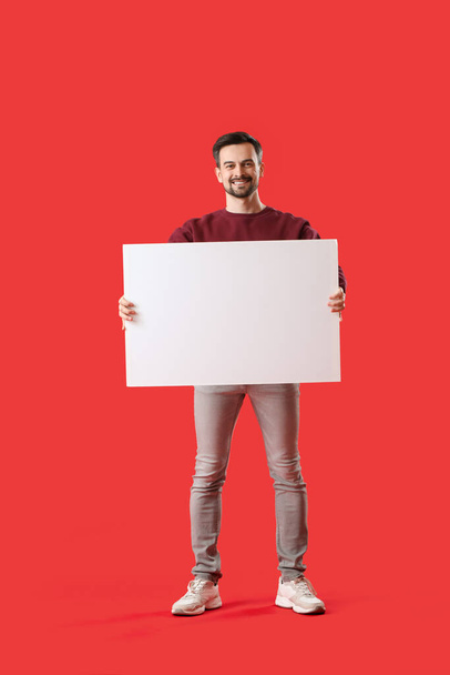 Schöner Mann mit großem leeren Poster auf rotem Hintergrund - Foto, Bild
