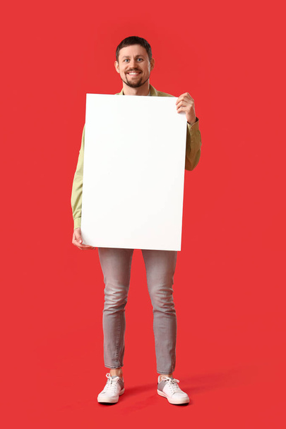 Handsome man with big blank poster on red background - Photo, Image