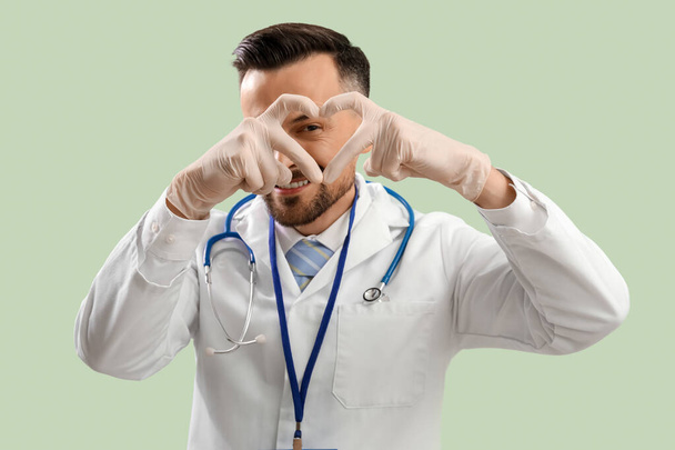Médico varón haciendo corazón con las manos sobre fondo verde - Foto, imagen